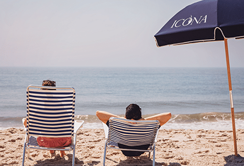 People looking out at the ocean in beach chairs under an ICONA umbrella