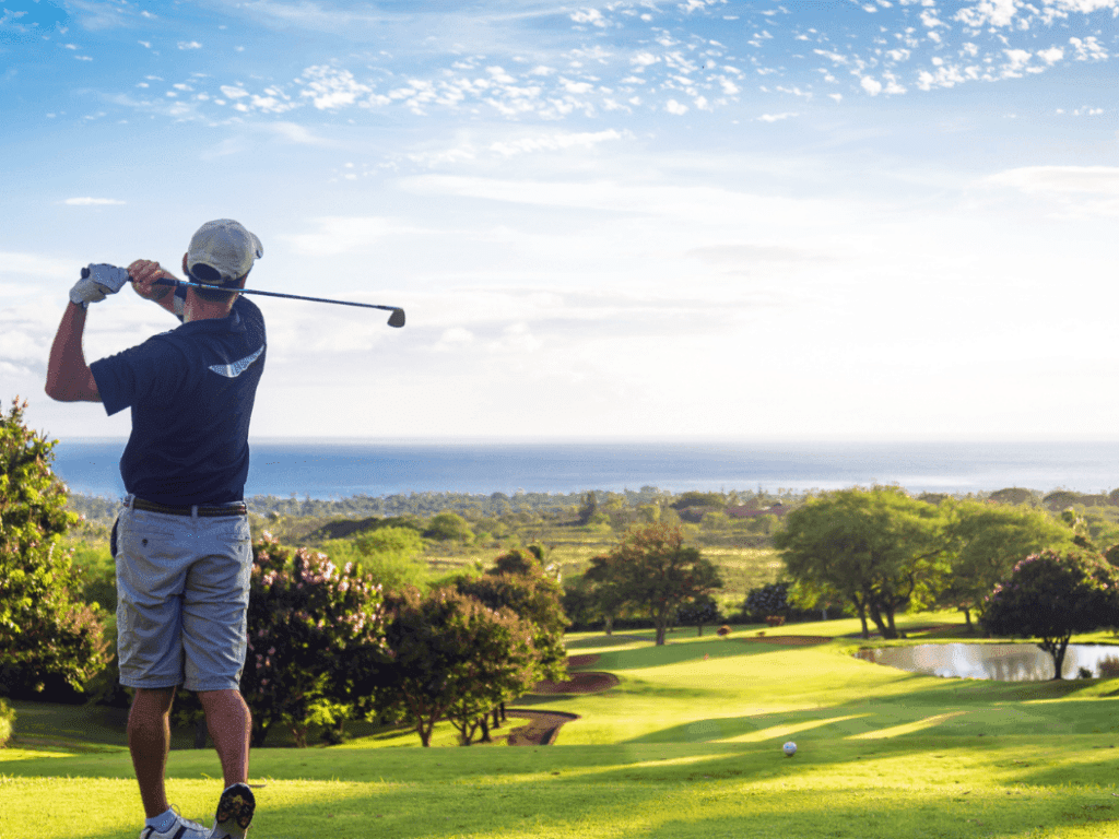 Man looking out at an ocean view while hitting a golf ball