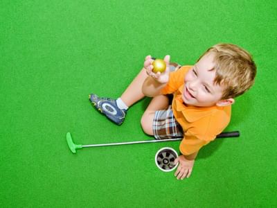 Young boy holding a golf ball and club on a mini-golf course