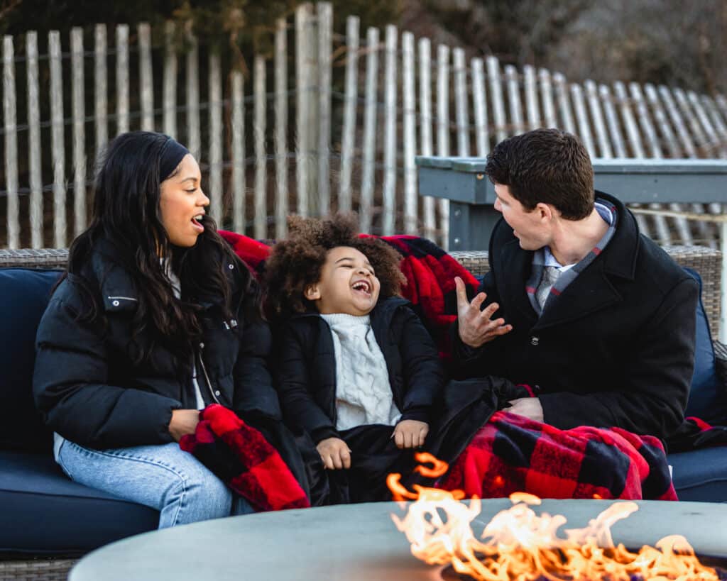 family of 3 laughing around the firepit at Winter Wonderland at the Sandbar in Avalon NJ