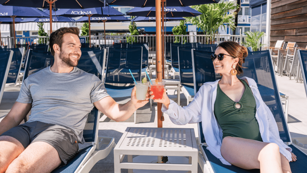 Couple toasting with drinks on lounge chairs next to ICONA's pool