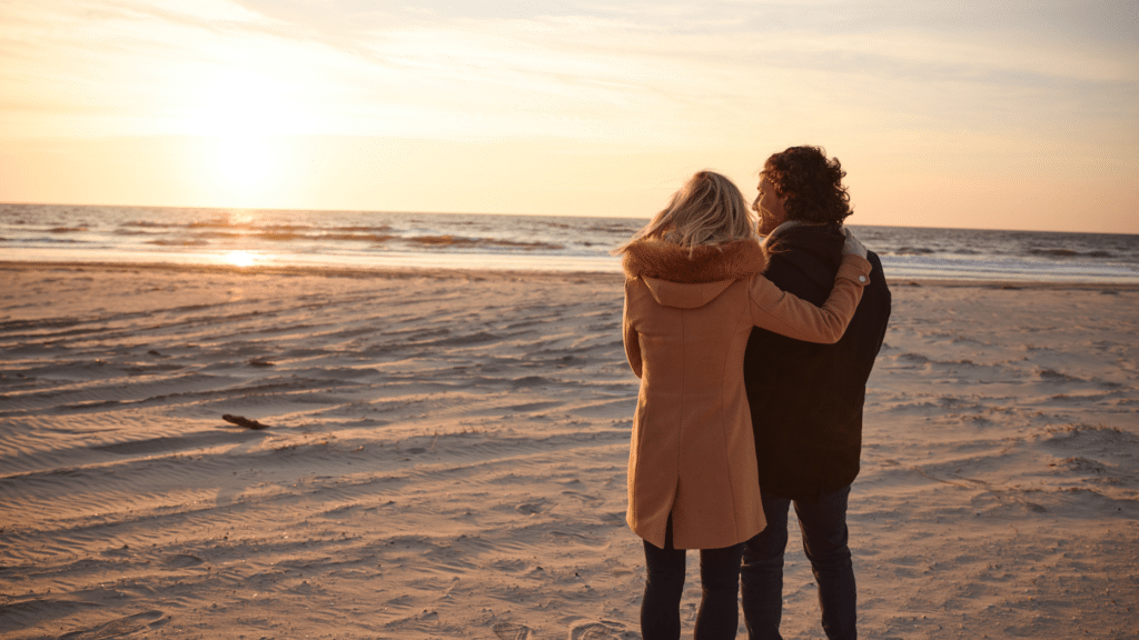 Couple embracing on the beach as they look out over the ocean